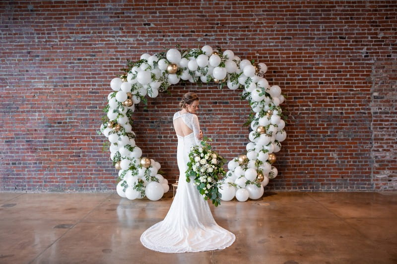 Bride standing in front of white balloon arch with foliage