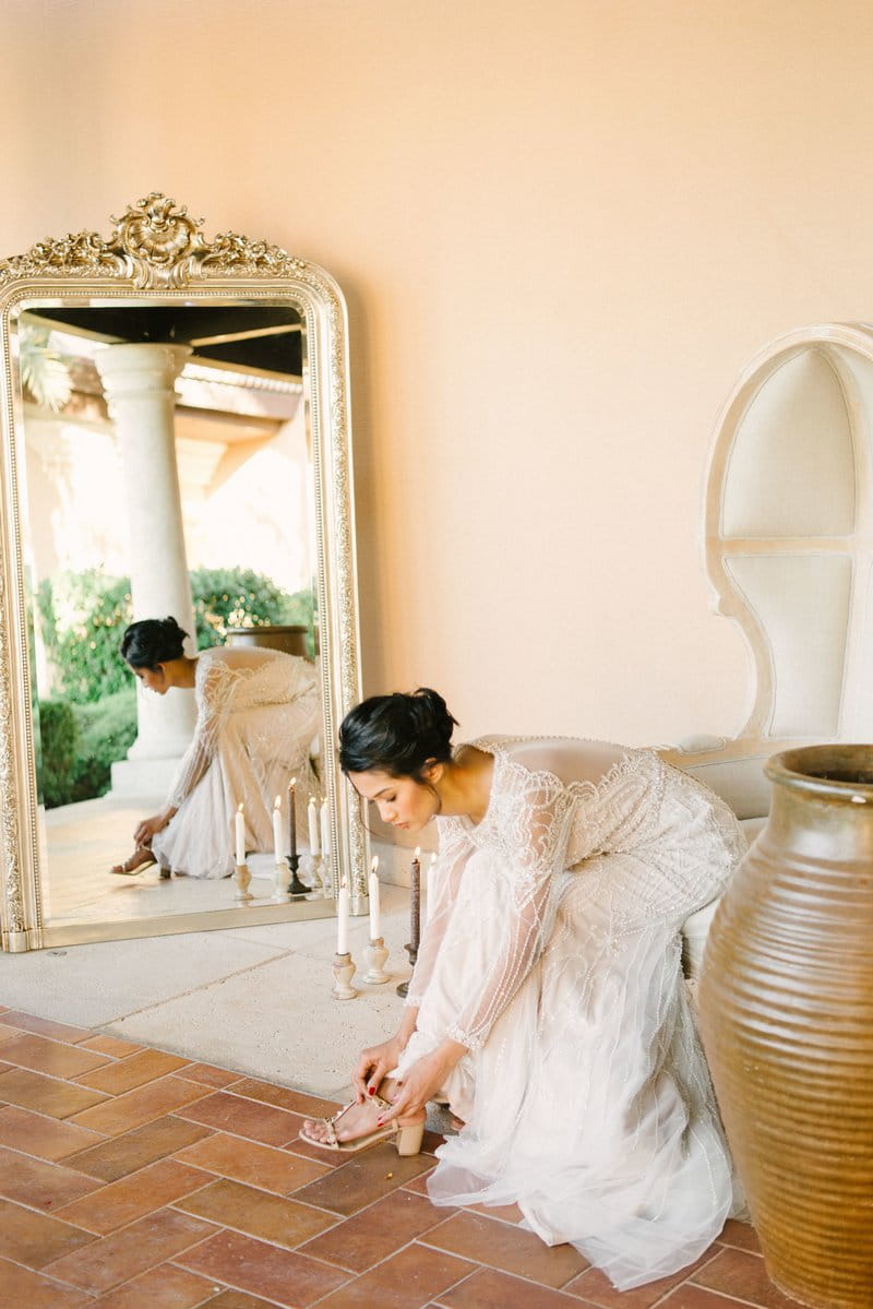 Bride leaning forward from chair to put on bridal shoes