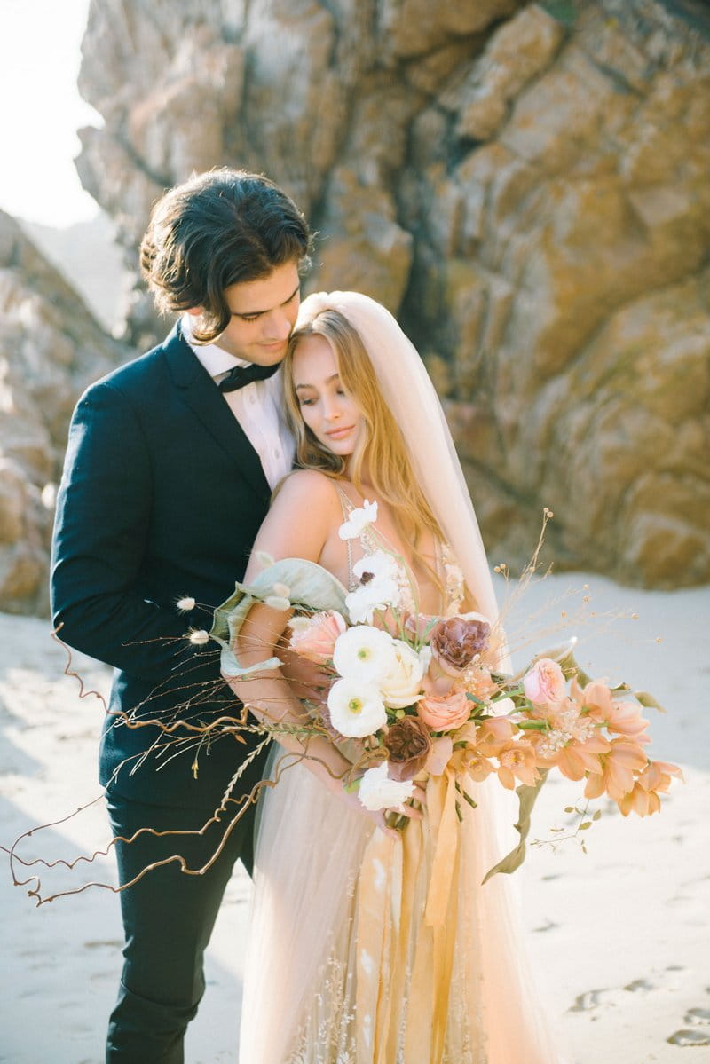 Groom standing behind bride on beach