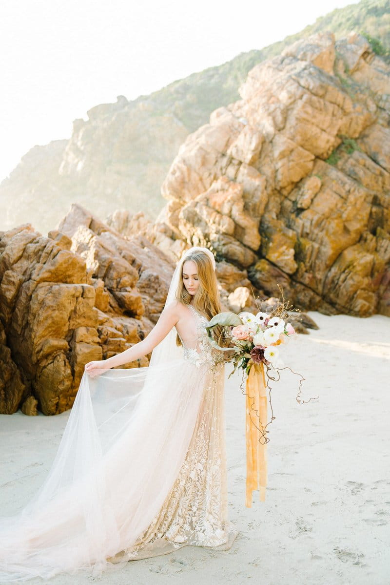 Bride holding out skirt of her wedding dress on beach