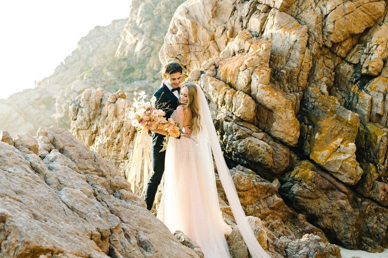 Bride and groom standing on rocks on beach