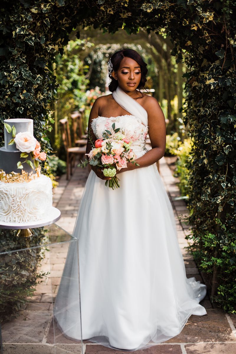 Bride standing holding bouquet next to wedding cake
