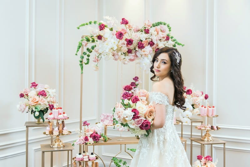 Bride holding pink bouquet in front of gold wedding dessert tables