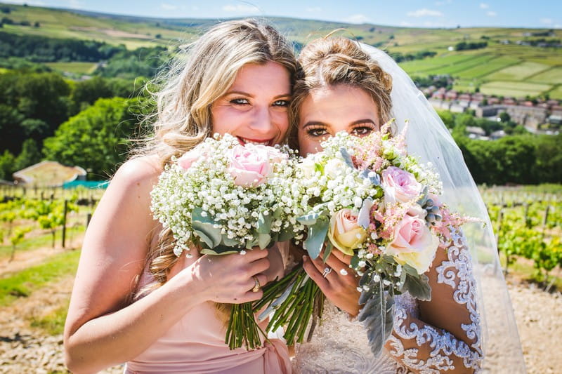 Bride and bridesmaid holding bouquets in front of faces