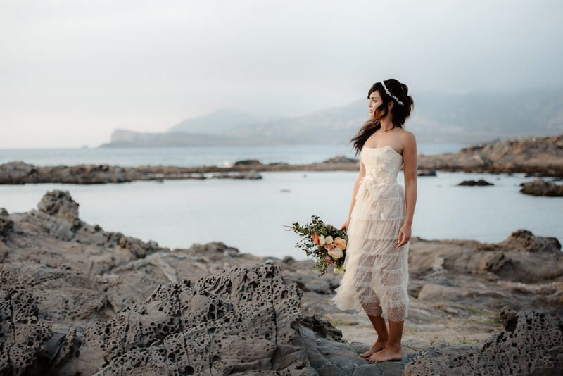 Boho bride holding bouquet looking out to sea