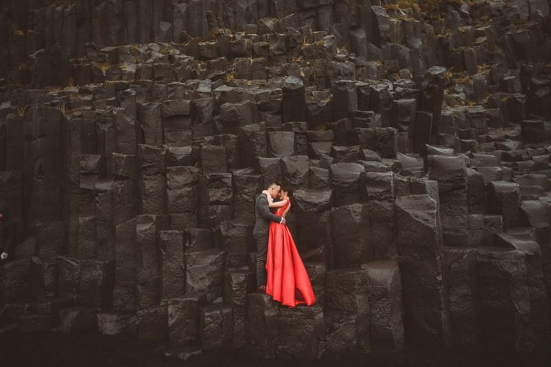 Bride and groom standing on edge of black rocks - Picture by Alexa Penberthy Photography