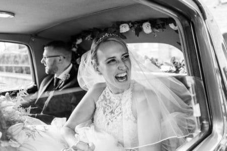 Happy bride with beaming smile in back of wedding car - Joss Denham Photography