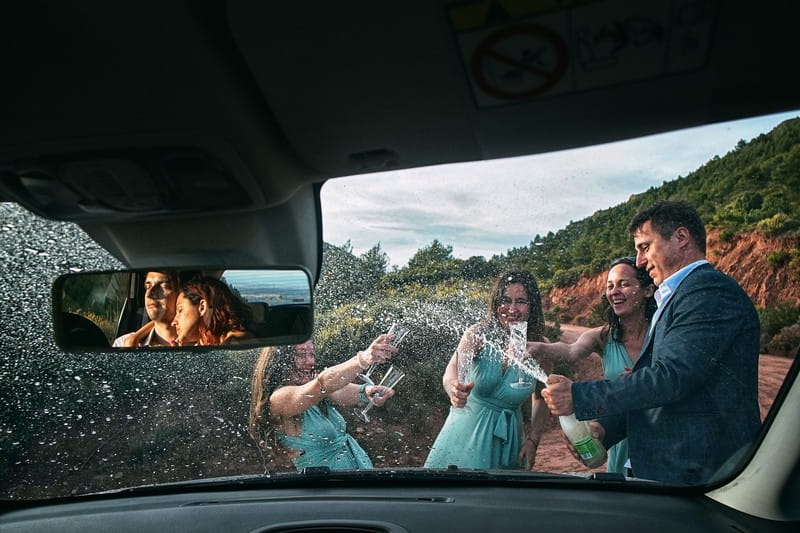 Man with bridesmaids spraying champagne with reflection of bride and groom in car mirror - Picture by Emin Kuliyev