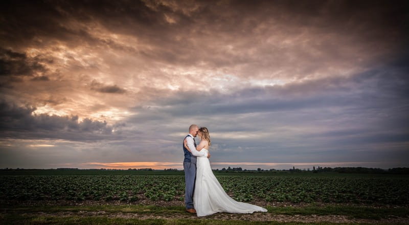 Bride and groom touching heads in a field with grey sky overhead - Picture by Peter Rollings Photography