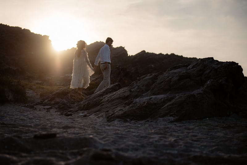 Couple walking across La Pelosa beach as sun goes down