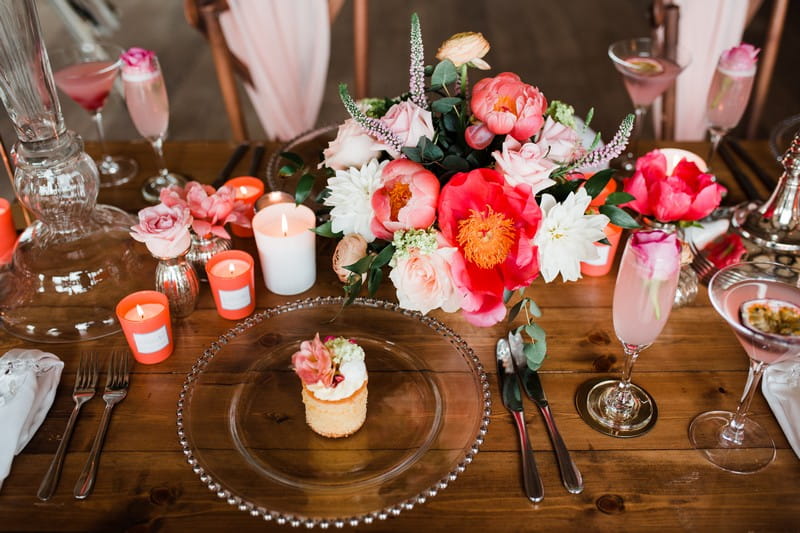 Small cake on clear plate and coral wedding table flowers and candles