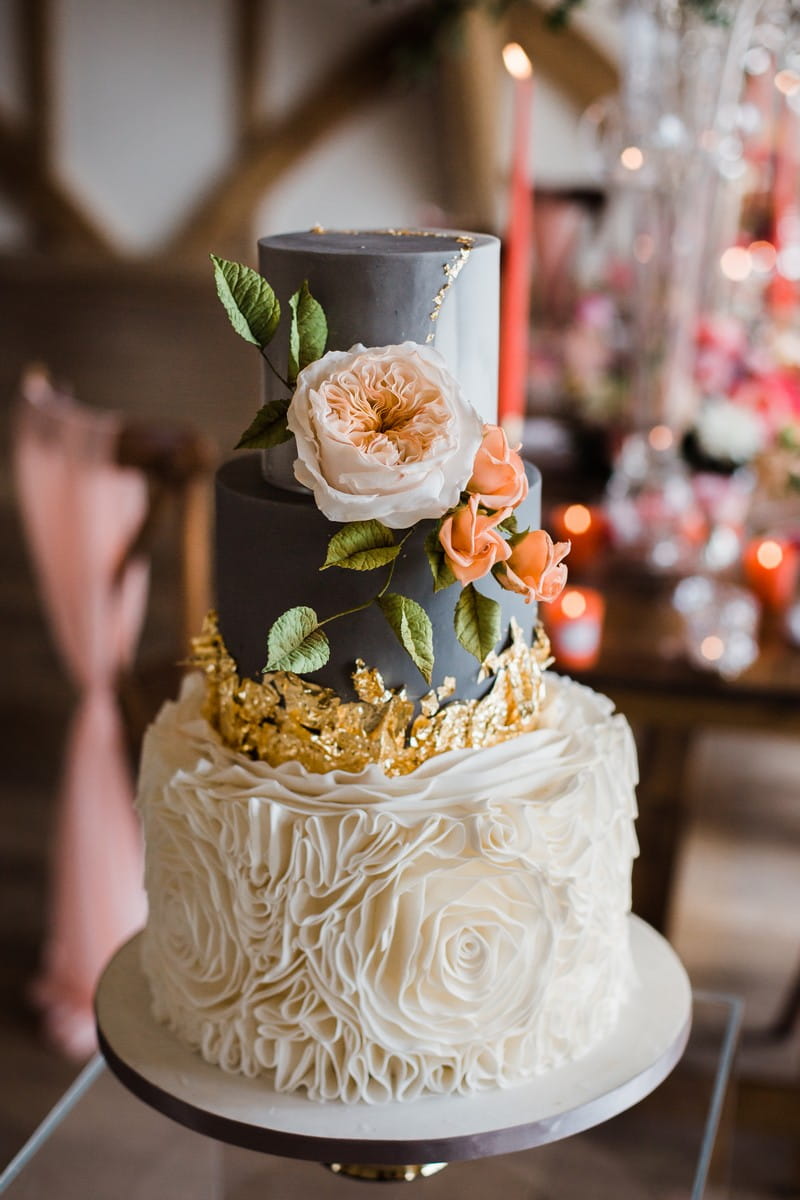 Grey and white wedding cake with coral flowers and gold leaf