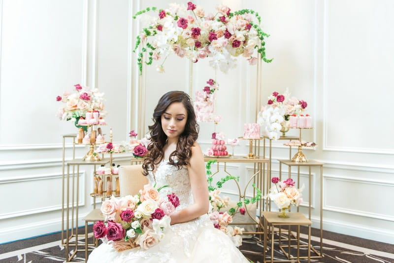 Bride sitting in front of dessert table styled with pink flowers