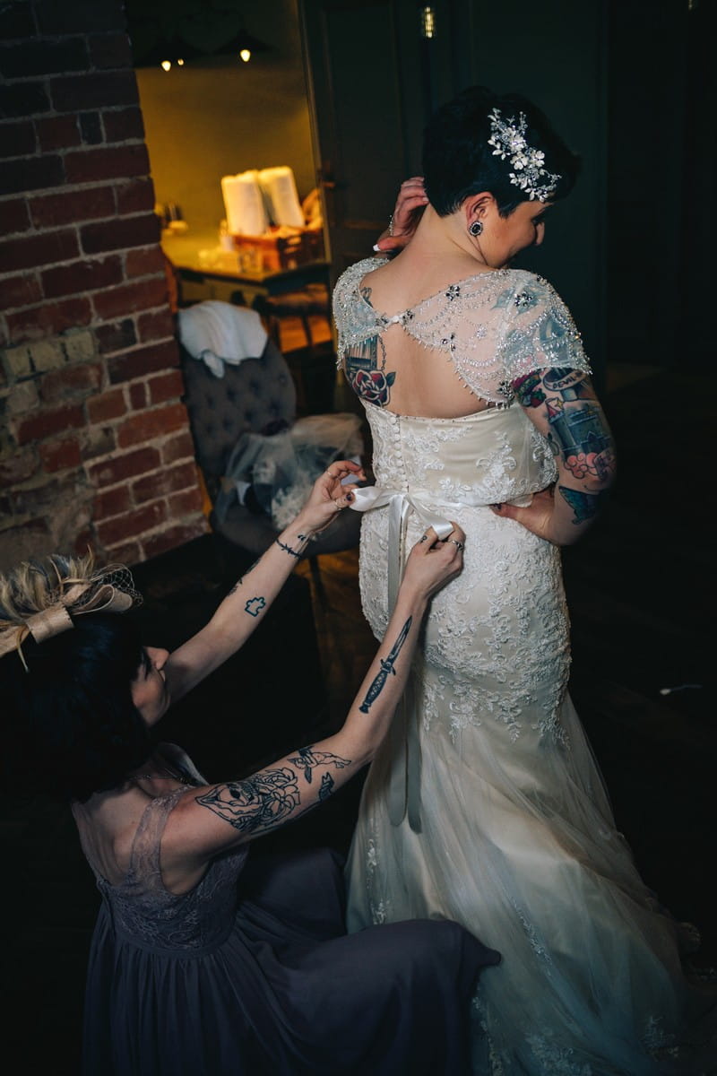 Lady with tattoos doing up back of bride's dress