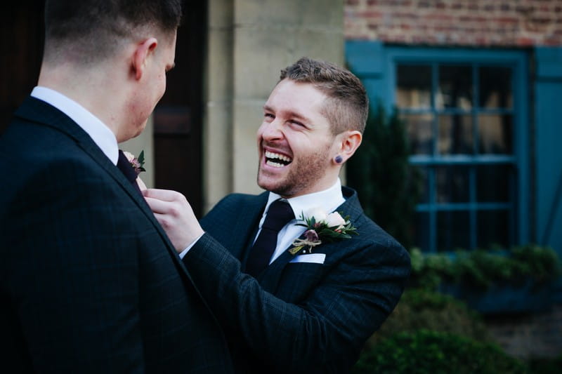 Groom with big smile as he adjusts best man's buttonhole