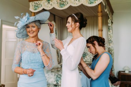 Bride combing mother's hair while bridesmaid does up the back of bride's dress - Picture by Eilidh Robertson Photography