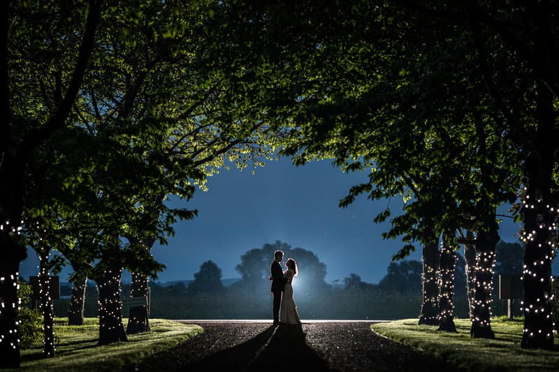 Bride and groom standing under trees at night - Picture by Rafe Abrook Photography