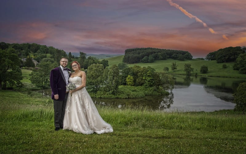 Bride and groom in front of lake and red sky - Picture by Image-i-Nation Photography