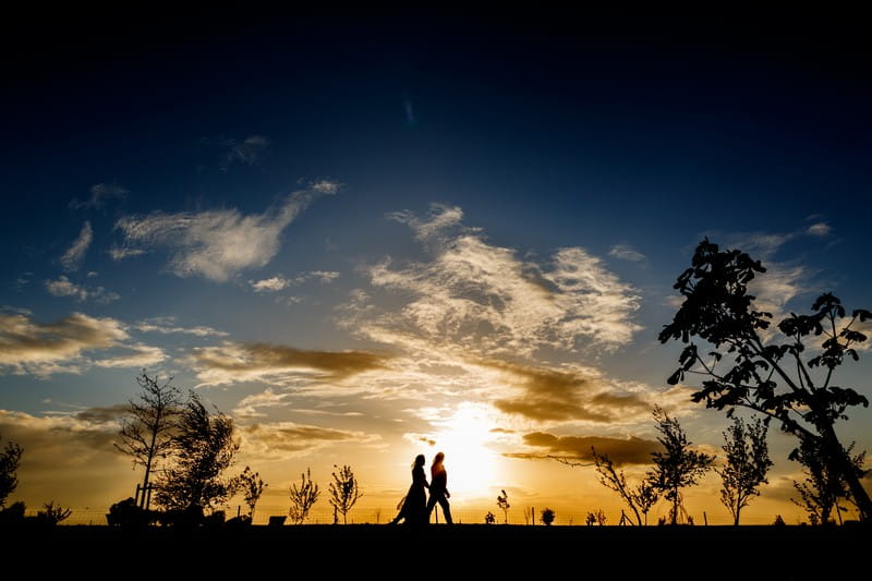 Silhouette of couple walking in front of brilliant yellow and blue sky from sunset - Picture by John Woodward Photography