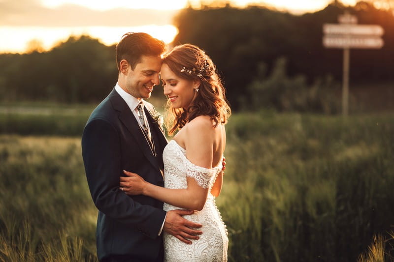 Bride and groom touching heads with field in background - Picture by Honeydew Moments