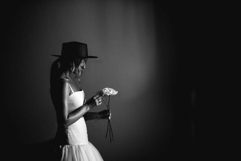 Bride wearing hat looking down at flower - Picture by That Moment Photo