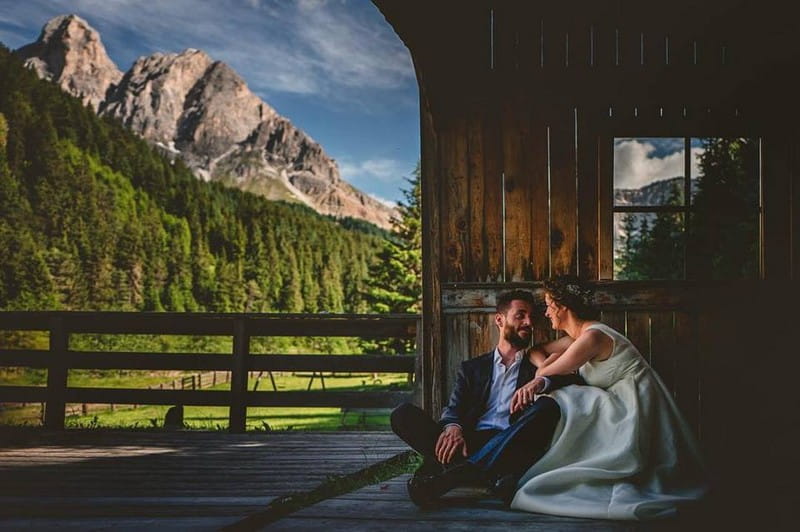 Bride and groom sitting with trees and mountains in background - Picture by Livio Lacurre Photography