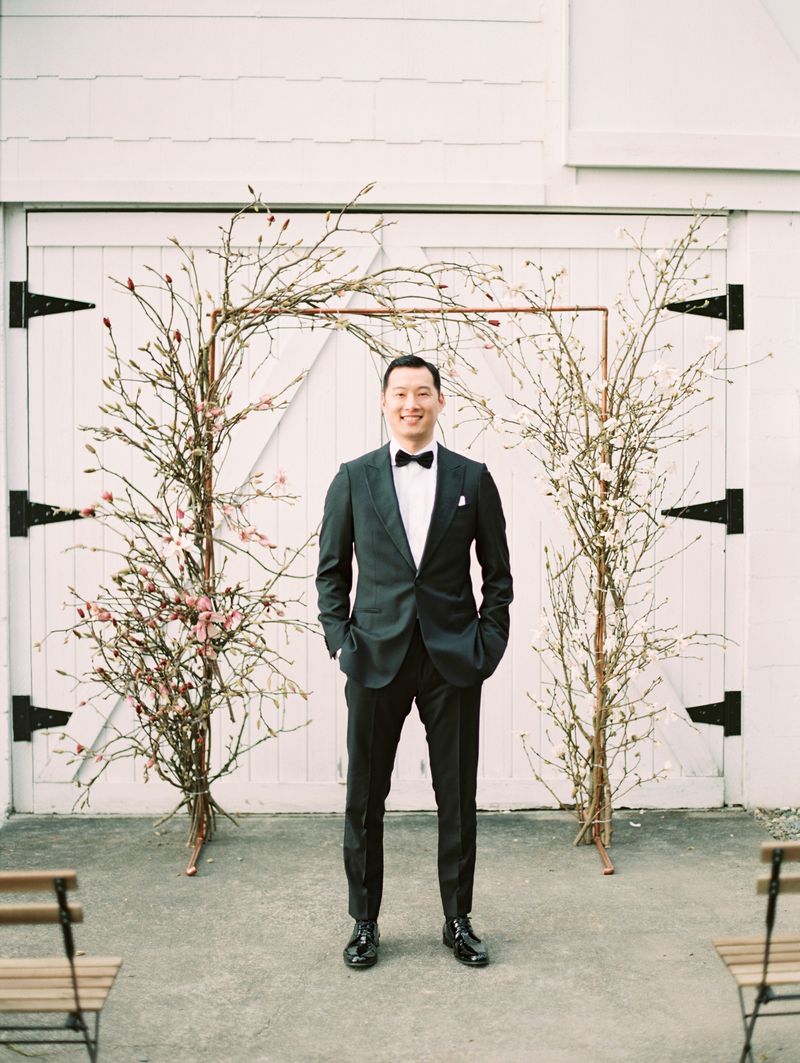 Groom standing in front of magnolia floral ceremony arch