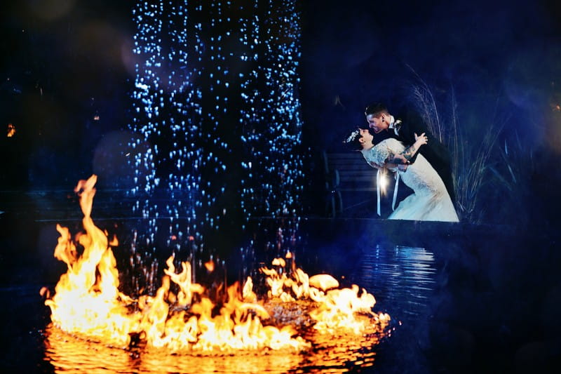 Bride and groom by fountain with fire around it at Le Petit Chateau