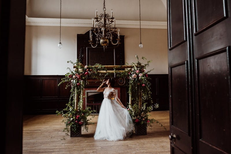 Bride in front of chuppah covered in foliage and peonies