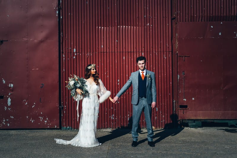Bride and groom holding hands in front of red outbuilding at Trenderway
