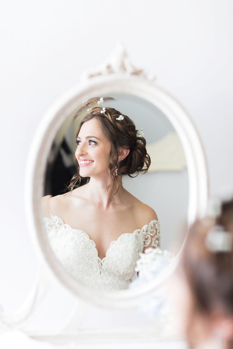 Reflection in mirror of bride looking to the side and smiling - Picture by First Light Photography