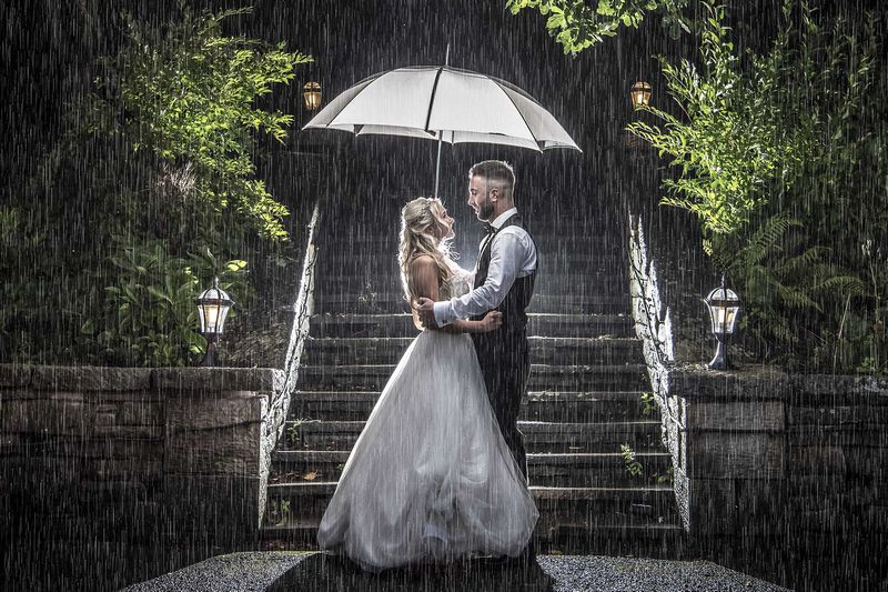 Bride and groom standing under umbrella in the rain - Picture by Peter Anslow Photography