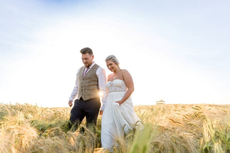 Bride and groom holding hands as they walk through a field of wheat - Picture by Heather Jackson Photography