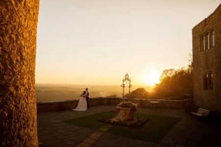 Bride and groom looking at view from courtyard of wedding venue as sun sets - Picture by Helen England Photography