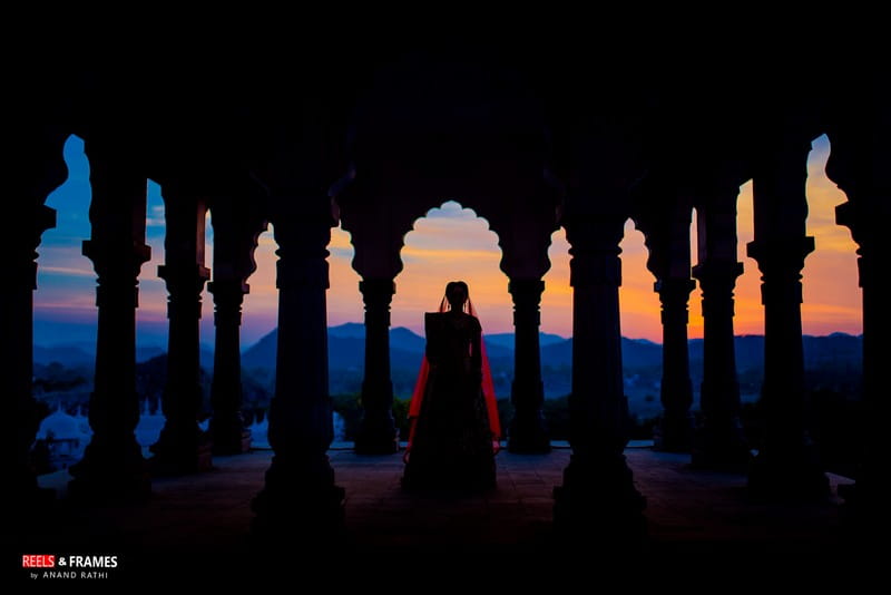 Silhouette of bride standing between pillars of wedding venue looking at views of mountains - Picture by Reels and Frames