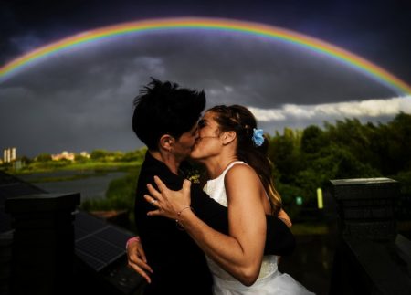 Two brides kissing with rainbow overhead - Picture by Jason Williams Photography