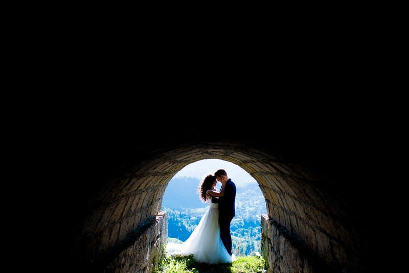Bride and groom at the end of dark tunnel in front of view of landscape - Picture by Victor Duduca