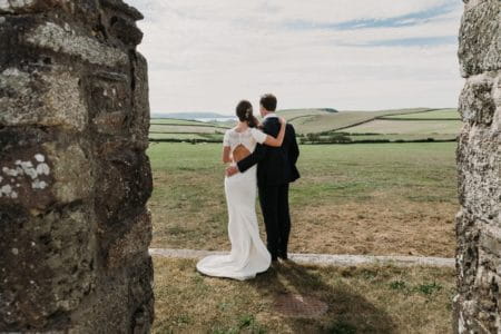 Bride and groom with arms on each others backs looking at view across field - Picture by Alexa Poppe Wedding Photography