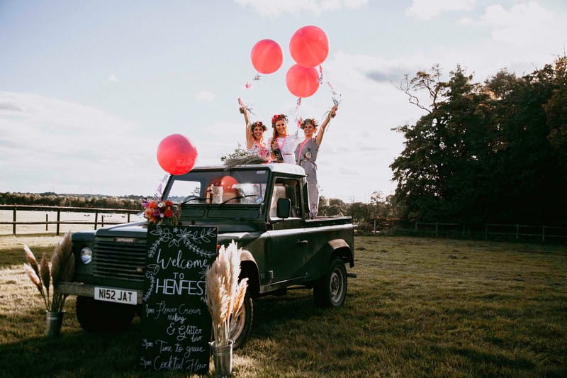 Henfest sign in front of girls standing on back of Land Rover holding balloons