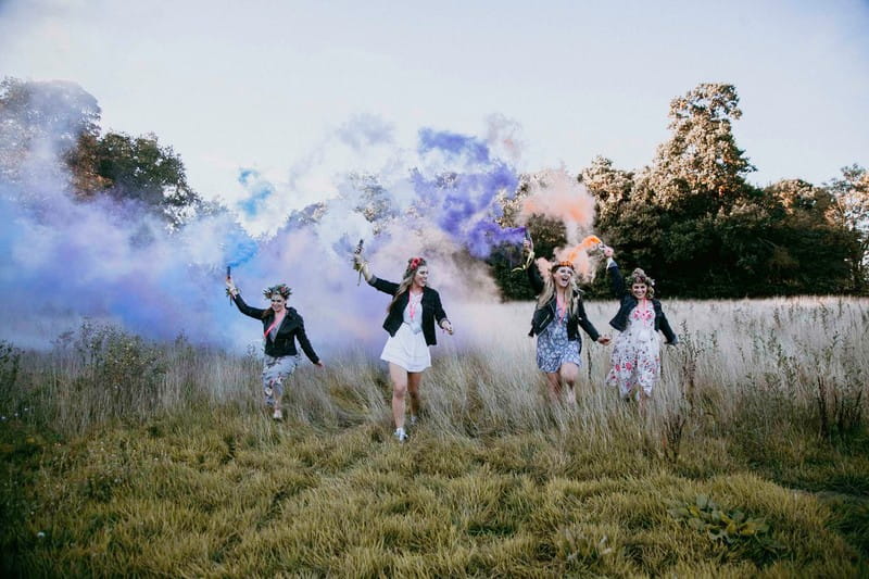 Girls at hen party walking across field with smoke bombs