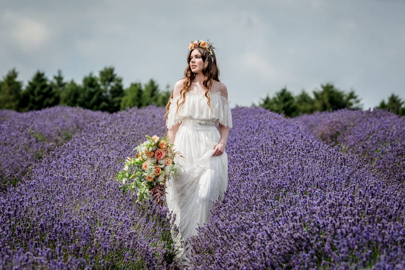 Bride holding up skirt as she walks through field of lavender