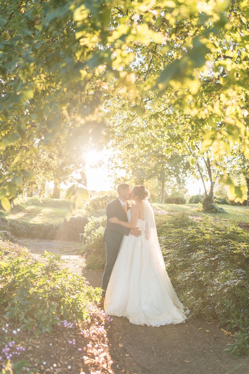 Bride and groom kissing under trees in hazy sunshine - Tanya Flannagan Photography