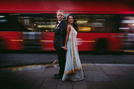 Bride and groom standing back to back with blurred red bus in background - Picture by Kevin Belson Photography