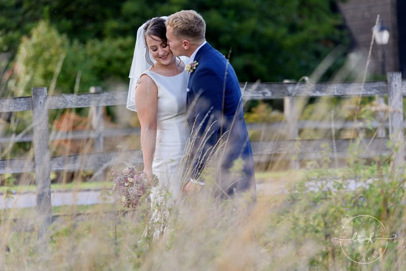 Groom kissing bride on cheek in field - Picture by Life Through A Lens - Rachel Ellis Photography