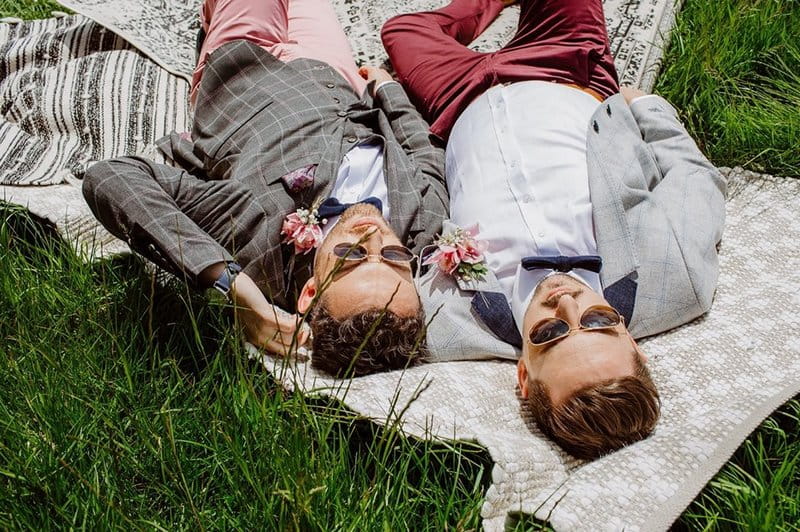 Two grooms with sunglasses on laying down next to each other on a rug - Picture by When Charlie Met Hannah