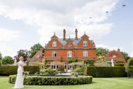 Bride standing by fountain of wedding venue as planes fly overhead - Picture by Heather Jackson Photography