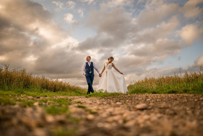 Bride and groom holding hands on path in countryside - Picture by Damian Burcher