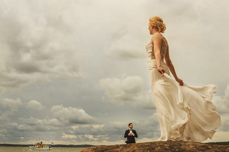 Bride standing looking out to sea with groom in background - Picture by Aleks Kus