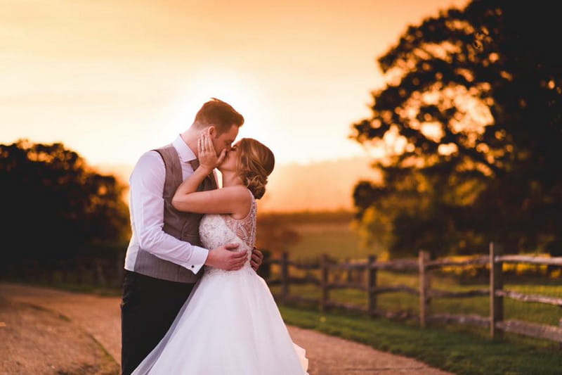 Bride and groom kissing in countryside as sun goes down - Picture by Sophie Oldhamstead Photography