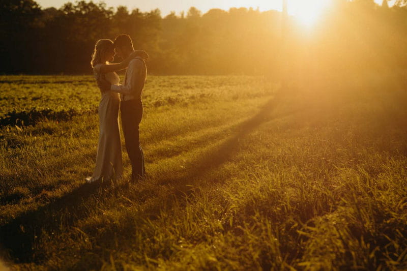 Bride and groom resting their heads against each other in field in hazy sunshine - Picture by Richard Skins Photography